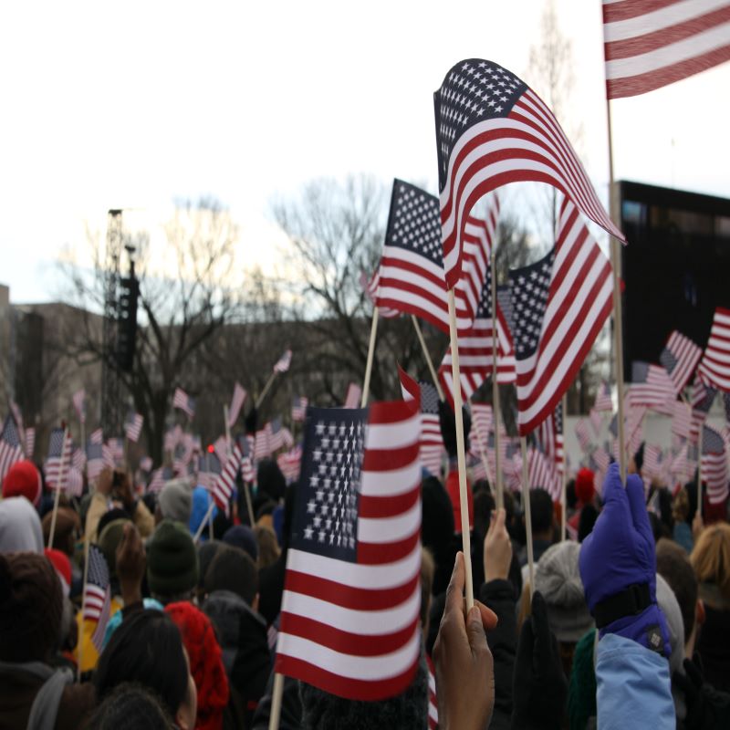 a crowd with american flags possibly reciting the pledge of allegiance